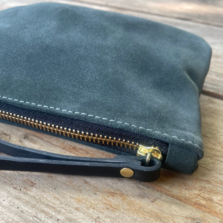 Spruce green suede pouch with gold zipper on a wooden surface